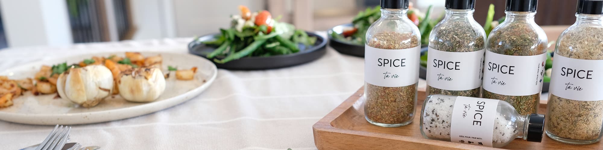 Plusieurs pots Spice ta vie présentés sur une table, entourés de mets